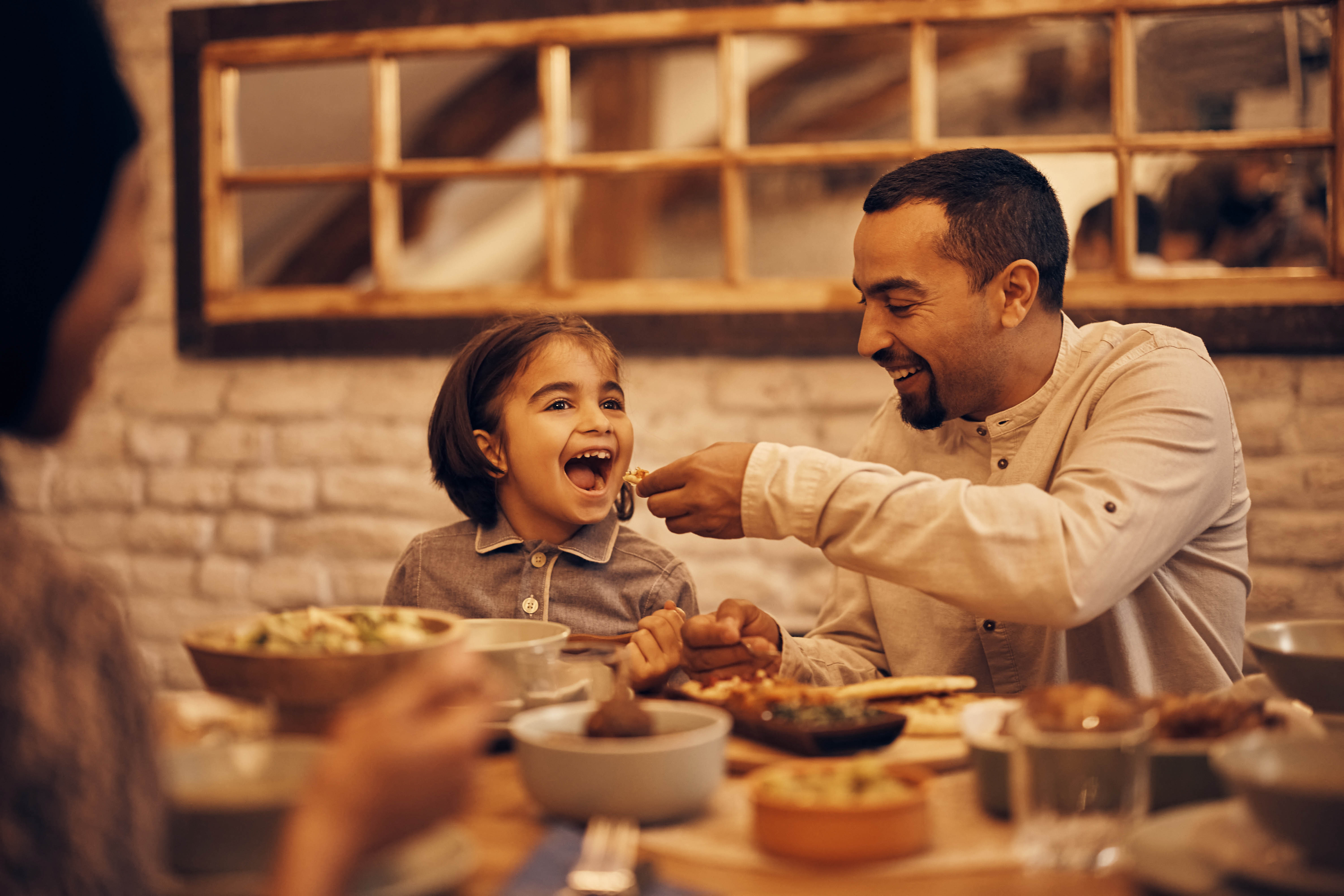 Dad feeding his daughter dinner at the table, picture looking in through the window Dad feeding his daughter dinner at the table, picture looking in through the window
